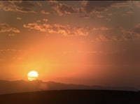the sun is setting over a hill with mountains in the background