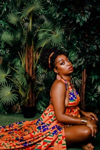 an african woman in an orange dress sitting on the ground