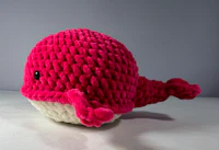 a pink crocheted whale stuffed animal on a white surface
