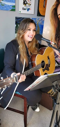 a woman playing an acoustic guitar in front of a microphone
