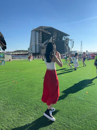 a woman in a red skirt is flying a bird in the grass