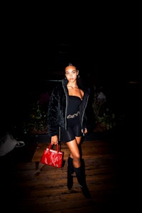 a woman in a black dress and black boots posing with a red purse