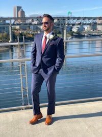 a man in a suit standing on a bridge near a river