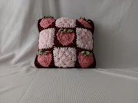 a pink and pink pillow with crocheted strawberries on it