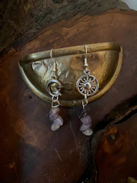 a pair of earrings with purple stones on a wooden plate