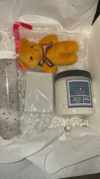 a gift box with a teddy bear and a candle