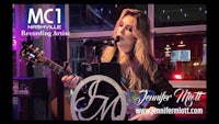 a woman is playing an acoustic guitar in front of a microphone