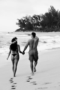 a black and white photo of a couple walking on the beach