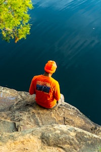 a man is sitting on a rock looking at the water