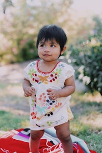 a baby girl in a mexican dress standing on a blanket
