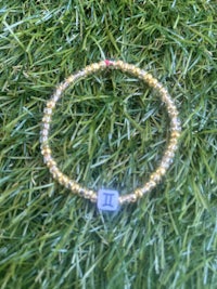 a gold beaded bracelet with the letter l on it