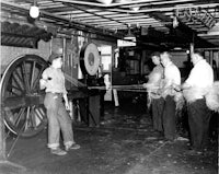 a group of men standing in a room with a wheel