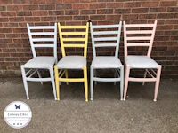 four pastel colored chairs in front of a brick wall