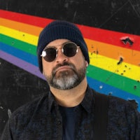 a man with a beanie and sunglasses is standing in front of a rainbow