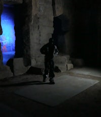 a man in leather pants leaning against a wooden wall