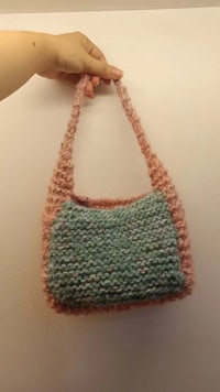 a hand holding a pink and green knitted bag