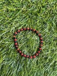 a red and black bead bracelet is laying on the grass