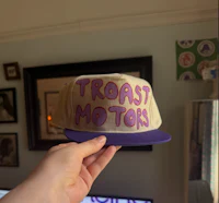 a person holding a hat that says toast motors
