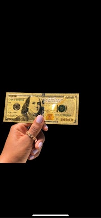 a person holding a gold dollar bill on a black background
