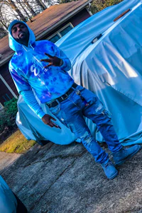 a man in a blue tie dye hoodie standing in front of a car