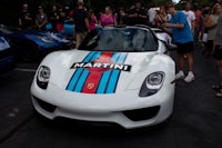 a white porsche sports car is parked in front of a crowd of people