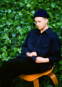a man wearing a black hat sitting on a wooden chair