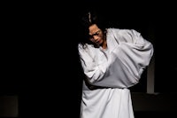 a man in a white robe is standing on a dark stage