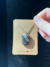 a hand holding a necklace with a stone on it