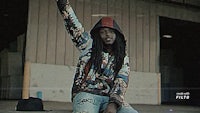 a man with dreadlocks and a hoodie is sitting on the ground