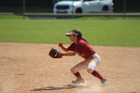 a softball player in a maroon uniform catching a ball