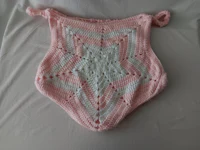 a pink and white crocheted blanket on a bed