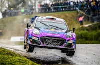 a rally car in the air over a muddy track