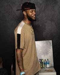 a man in a tan shirt with tattoos and a hat