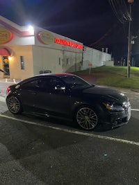 a black audi tt parked in front of a store at night