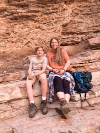 a woman and her son sitting on a rock in a canyon