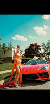 a woman in an orange dress posing next to a sports car
