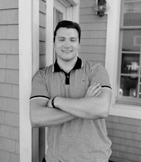 black and white photo of a man leaning against a house