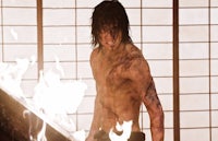 a man with no shirt standing in front of a fire
