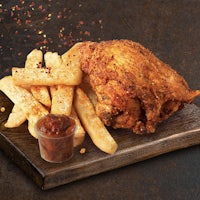 a chicken with fries and sauce on a wooden board
