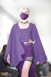 a woman wearing a purple cape and mask on the runway