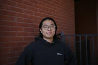 a man in a black hoodie standing in front of a brick wall