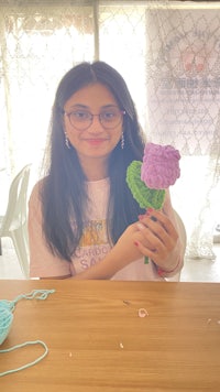 a girl is holding a flower made of yarn