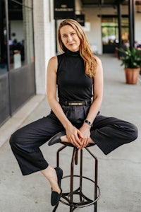 a woman sitting on a stool in a black top and black pants