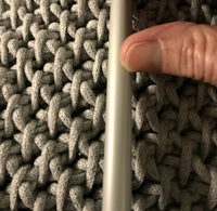 a person is holding a knitting needle in a grey yarn