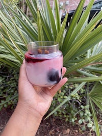 a hand holding a glass with a purple liquid in it