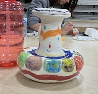 a woman is painting a vase on a table