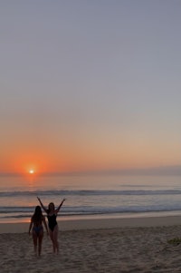 two women standing on the beach at sunset