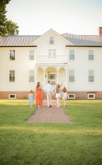 a family walks down a path in front of a large white house