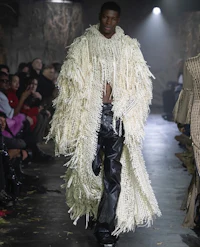 a model walks down the runway in a fur coat and leather pants