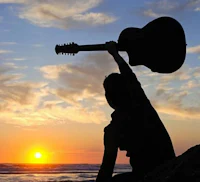 a man holding an acoustic guitar at sunset